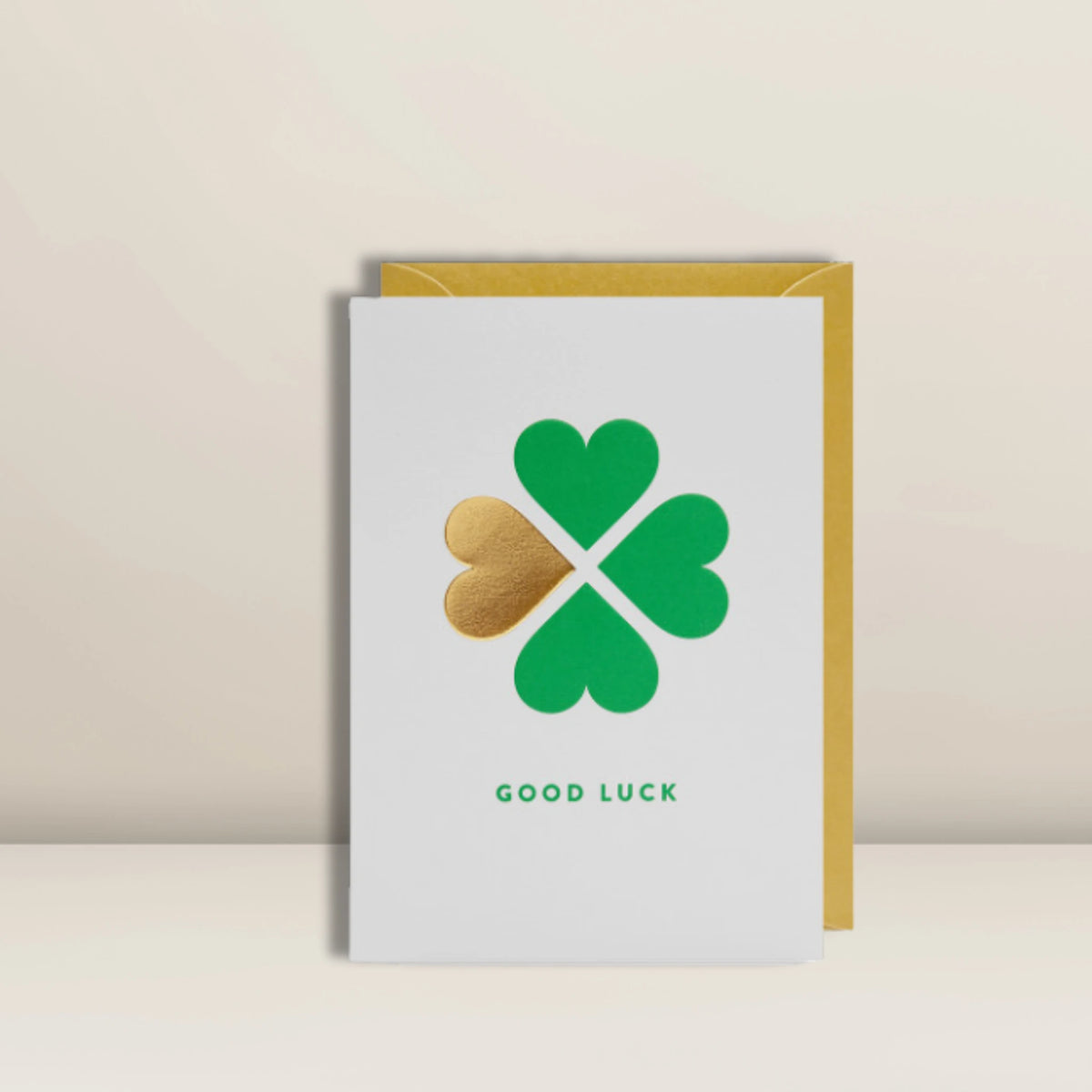 Eine Glückwunschkarte von Pacster mit dem Namen „Good Luck | Grußkarte“, die mit einem grünen und goldenen Kleeblatt-Motiv verziert ist und darunter den Schriftzug „GOOD LUCK“ trägt, steht vor einem gelben Umschlag auf neutralem Hintergrund. Entdecke hochwertige Geschenkideen bei Pacster.