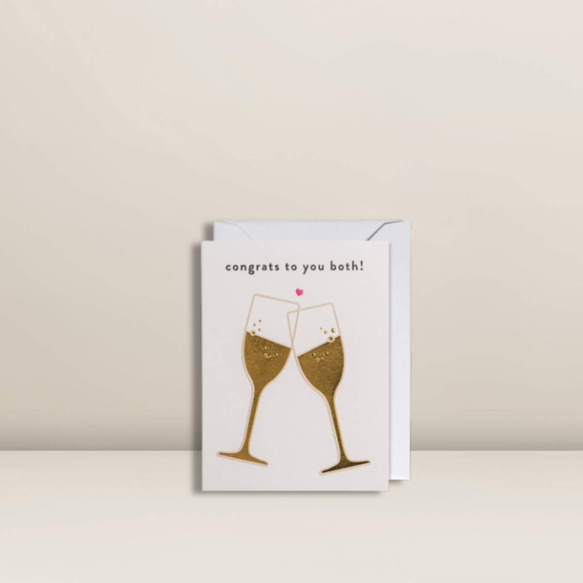 Mini-Grußkarte von Pacster mit zwei goldenen Champagnergläsern, die anstoßen, einem pinkfarbenen Herz darüber und dem Schriftzug „Congrats to you both!“ oben. Die „Congrats To You Both!“ | Mini-Grußkarte eignet sich perfekt für Hochzeitsglückwünsche und wird zusammen mit einem Umschlag vor neutralem Hintergrund präsentiert. Entdecke hochwertige Geschenkideen bei Pacster.